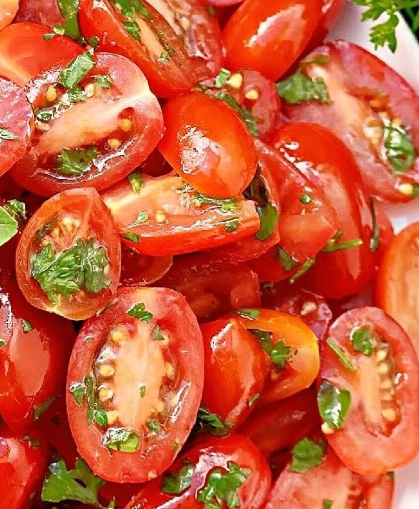 Close-up of halved grape tomatoes dressed with vinaigrette and sprinkled with fresh herbs.