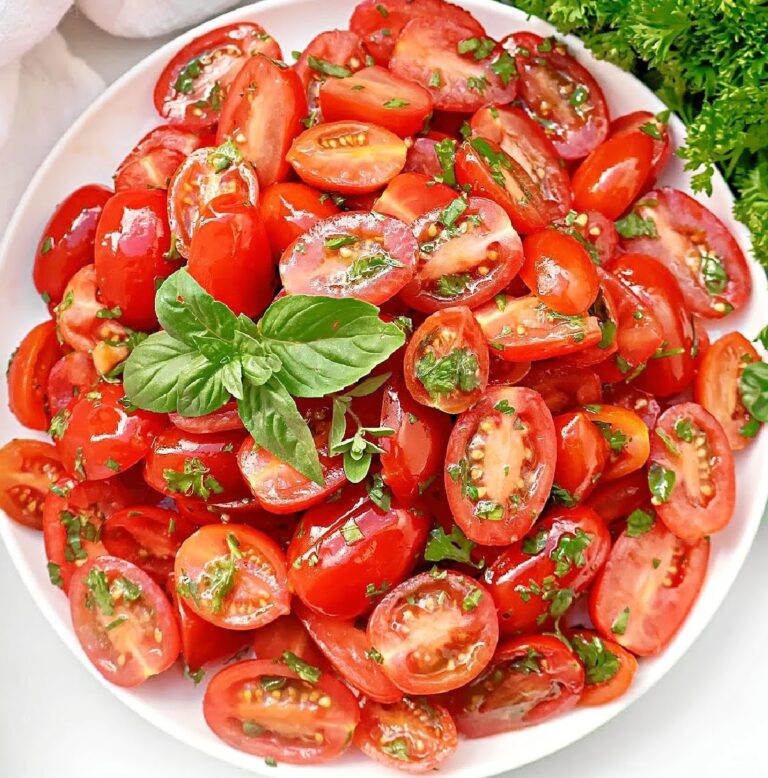 Close-up of a fresh tomato salad with fresh herbs, and a simple vinaigrette dressing in a white bowl.