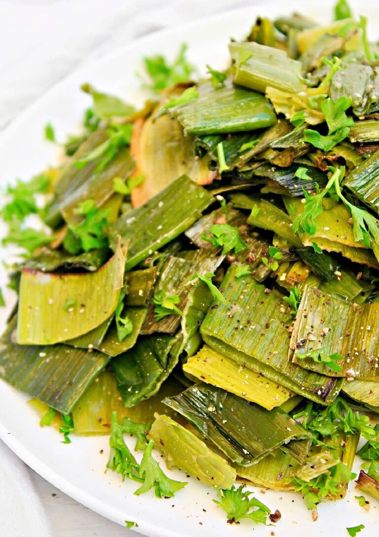 Partial side view of roasted leek salad on white plate.
