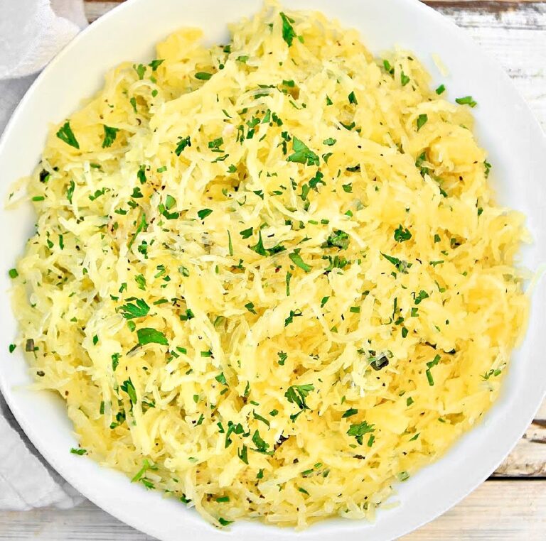 Top down view of white bowl filled with cooked spaghetti squash sprinkled with fresh herbs.