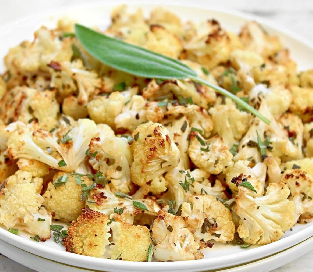 Plate of toasted cauliflower with flecks of fresh sage. A whole sage leaf is placed on top as a garnish.
