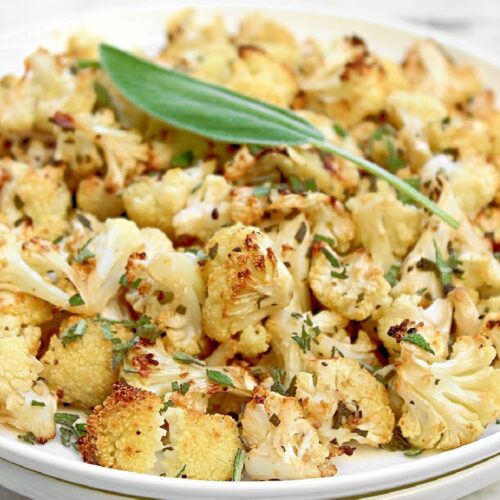Plate of toasted cauliflower with flecks of fresh sage. A whole sage leaf is placed on top as a garnish.