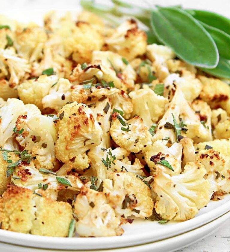 Close-up of roasted cauliflower, lightly charred and with chopped fresh sage visible throughout. Fresh sage leaves shown in top right corner.