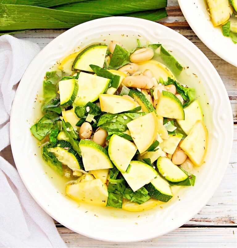 Soup with yellow squash, zucchini, white beans, and spinach in a white serving bowl.