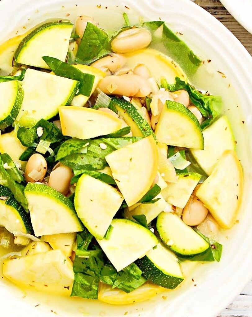 Soup with yellow squash, zucchini, white beans, and spinach in a white serving bowl.